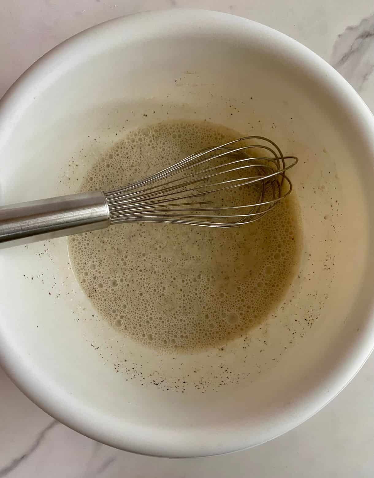 A bowl with a whisk and dressing mixed for American Cole Slaw.