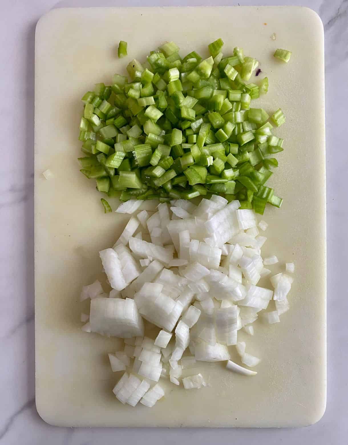 A cutting board with diced onion and celery.