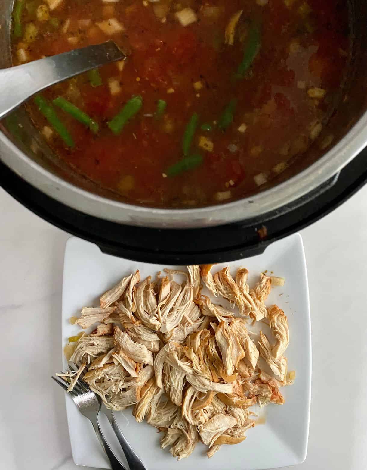 A slow cooker of soup and a plate with the chicken removed and shredded.