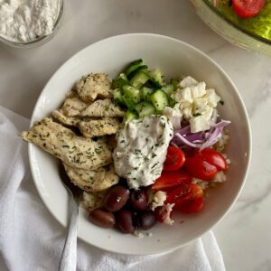 A Chicken Tzatziki Bowl with cauliflower rice, cooked chicken, olives, cucumbers, feta, tomatoes, red onion and tzatziki sauce.