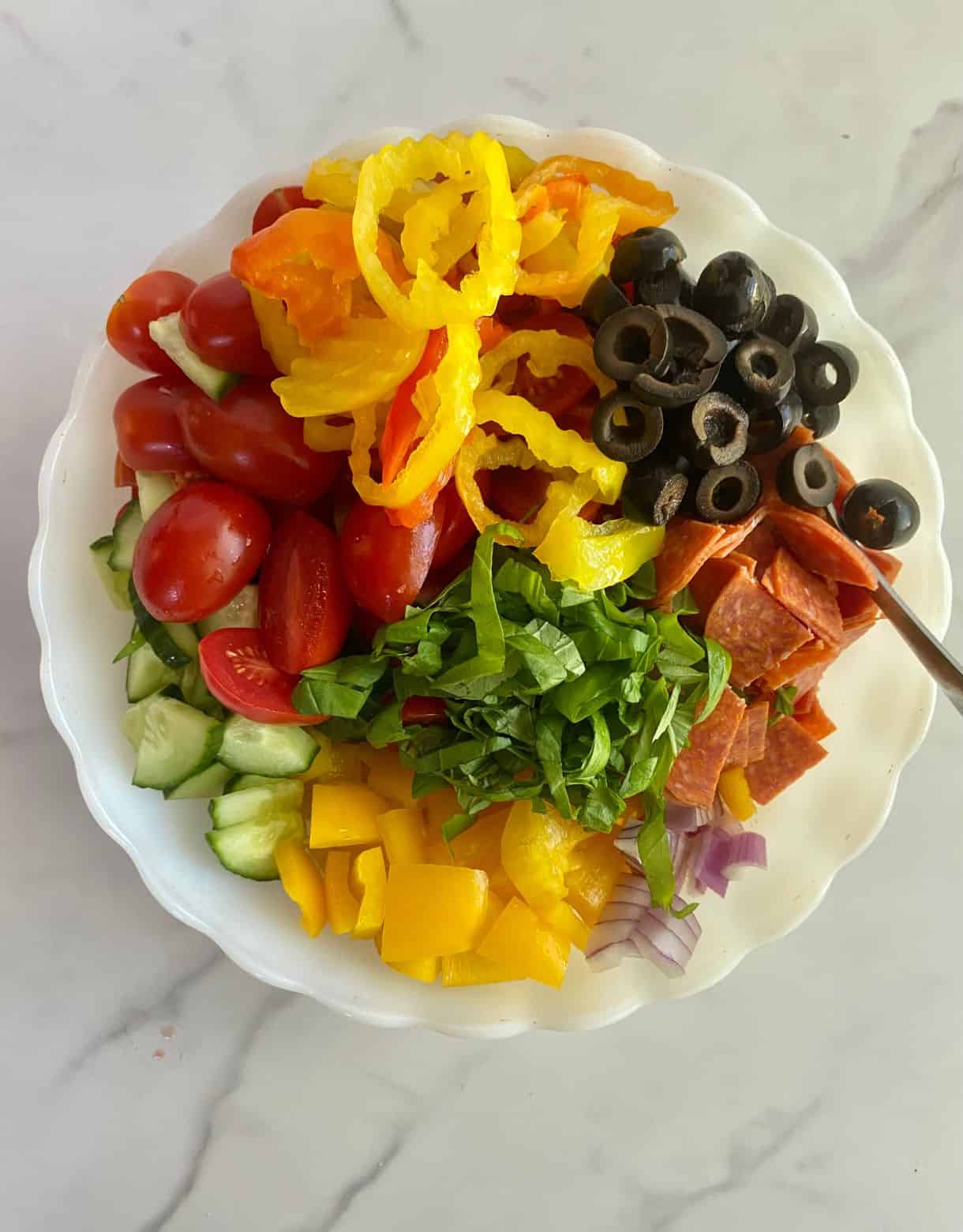 A bowl with ingredients added for Chopped Italian Salad but not yet stirred.