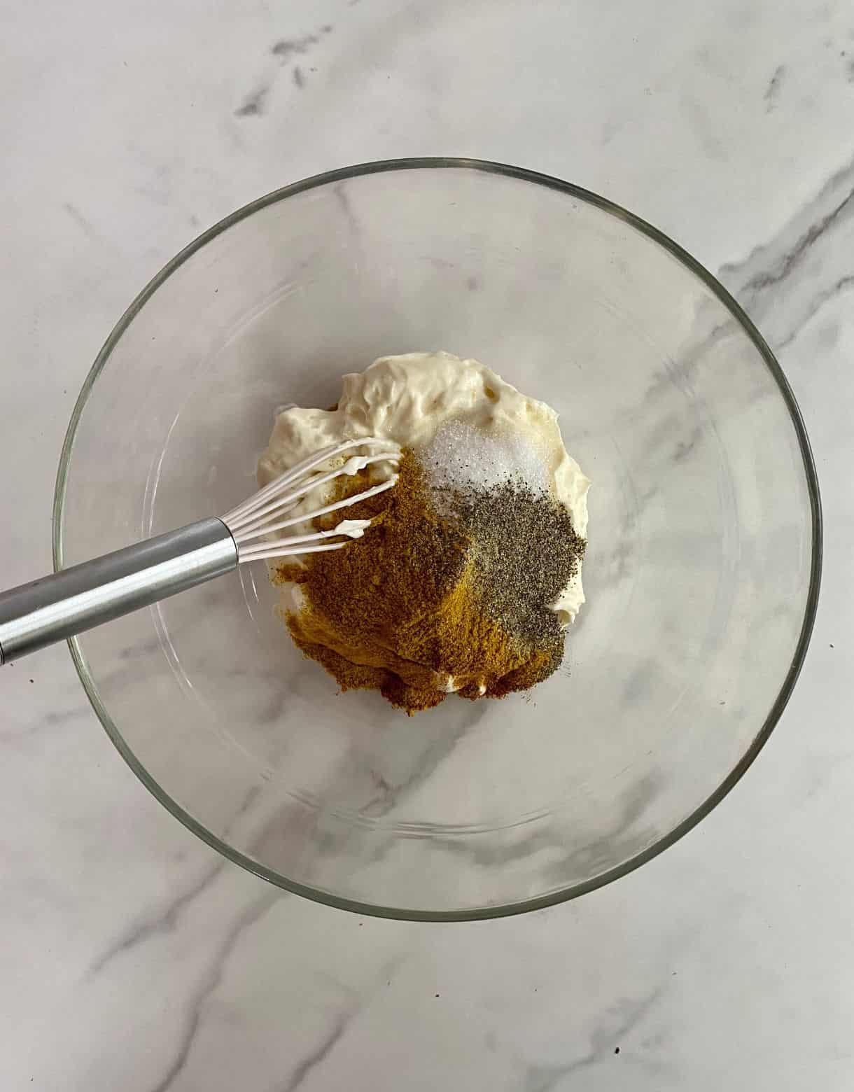 a bowl with mayonnaise, curry powder, salt, pepper, sugar and a whisk ready to mix.