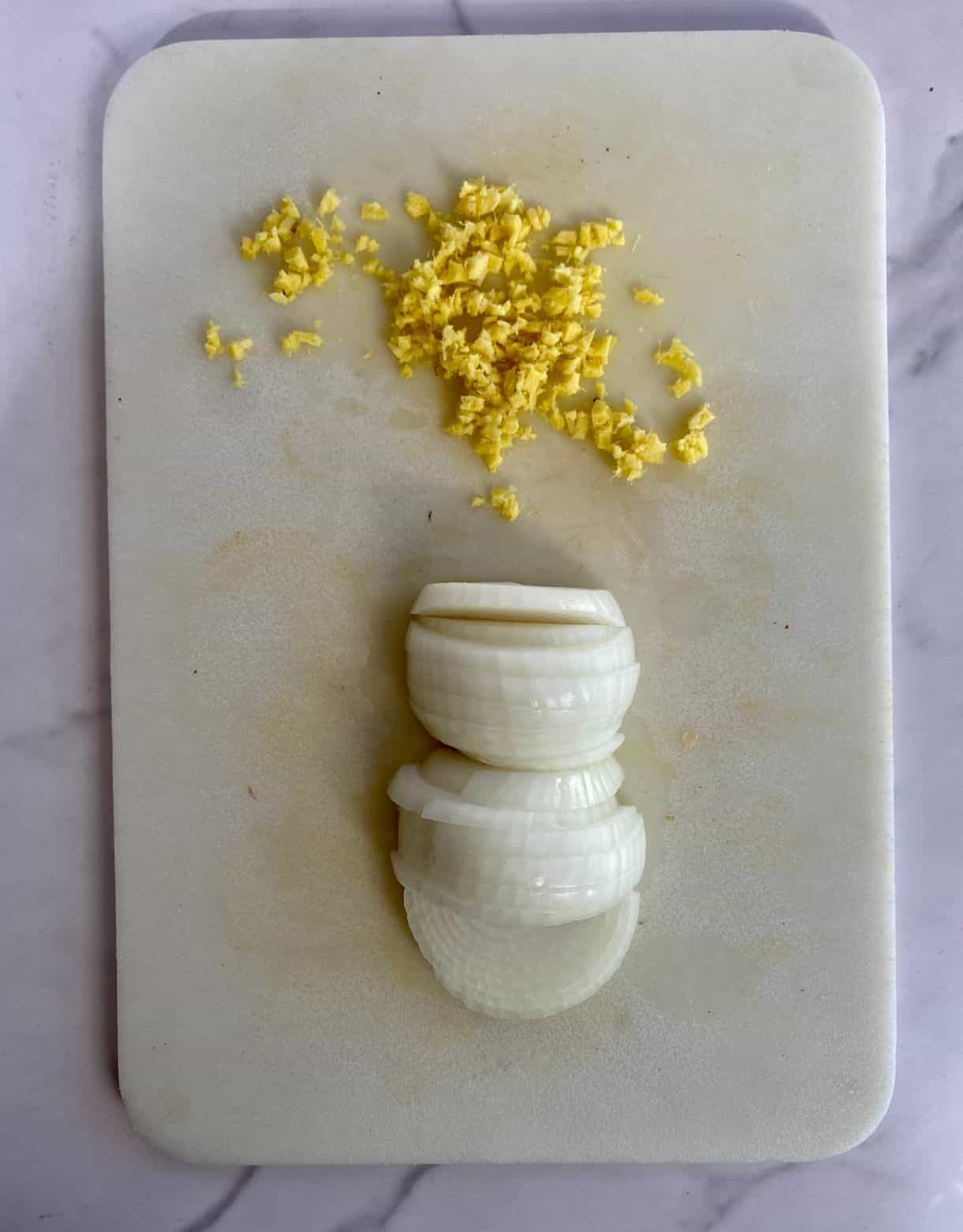 A cutting board with sliced onion and minced ginger.