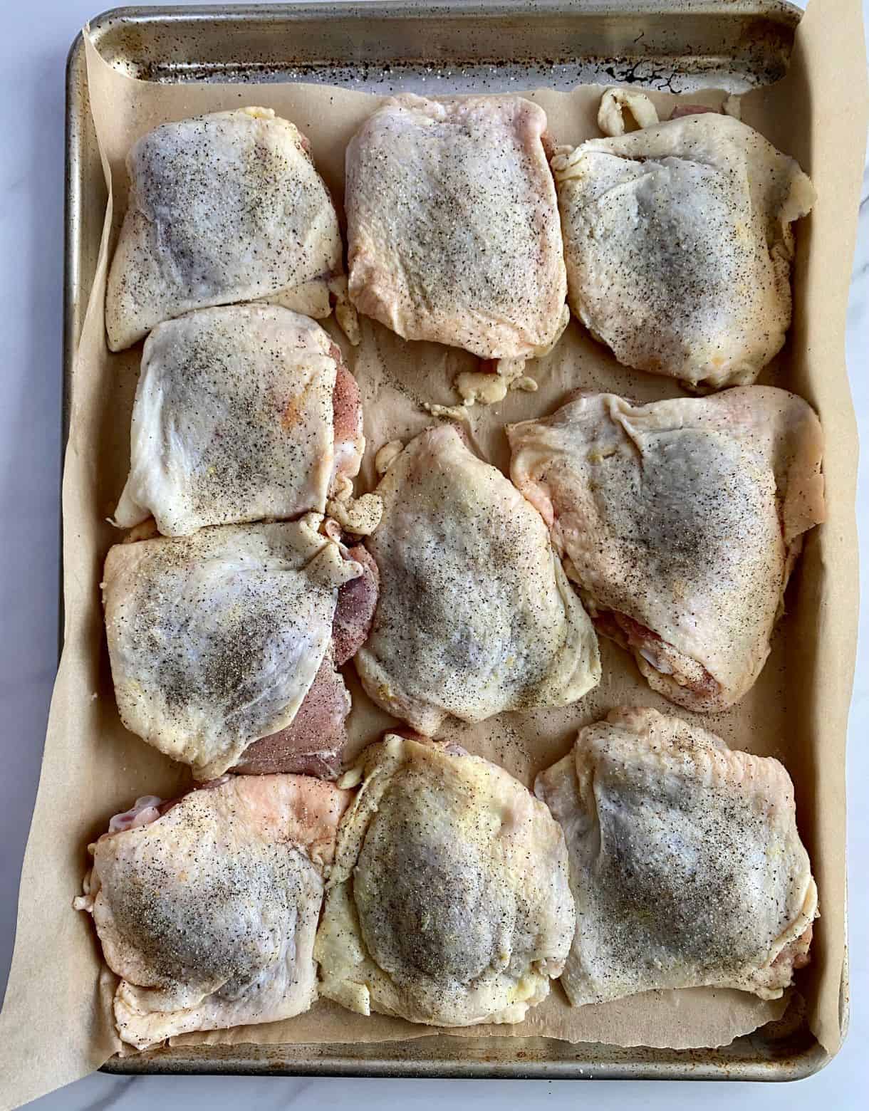 A sheet pan with season raw chicken thighs ready to go in the oven.