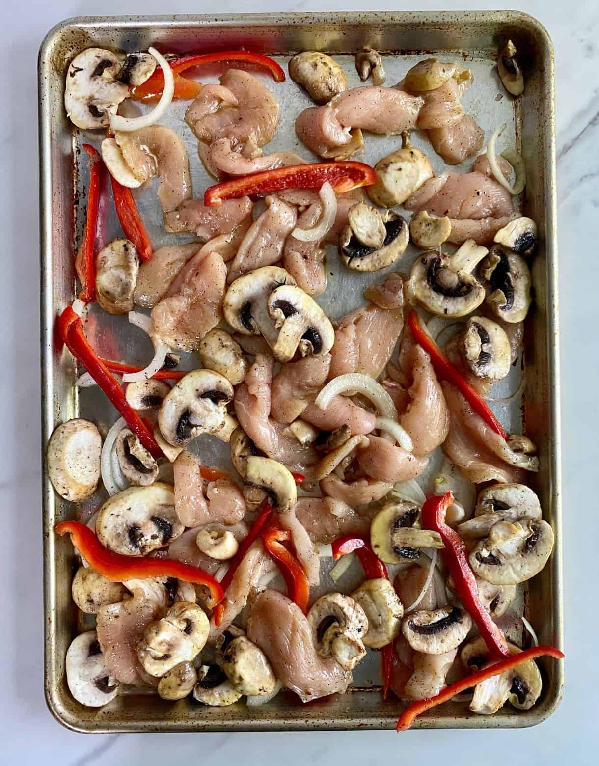 A sheet pan with raw chicken, onions, mushrooms and bell pepper.