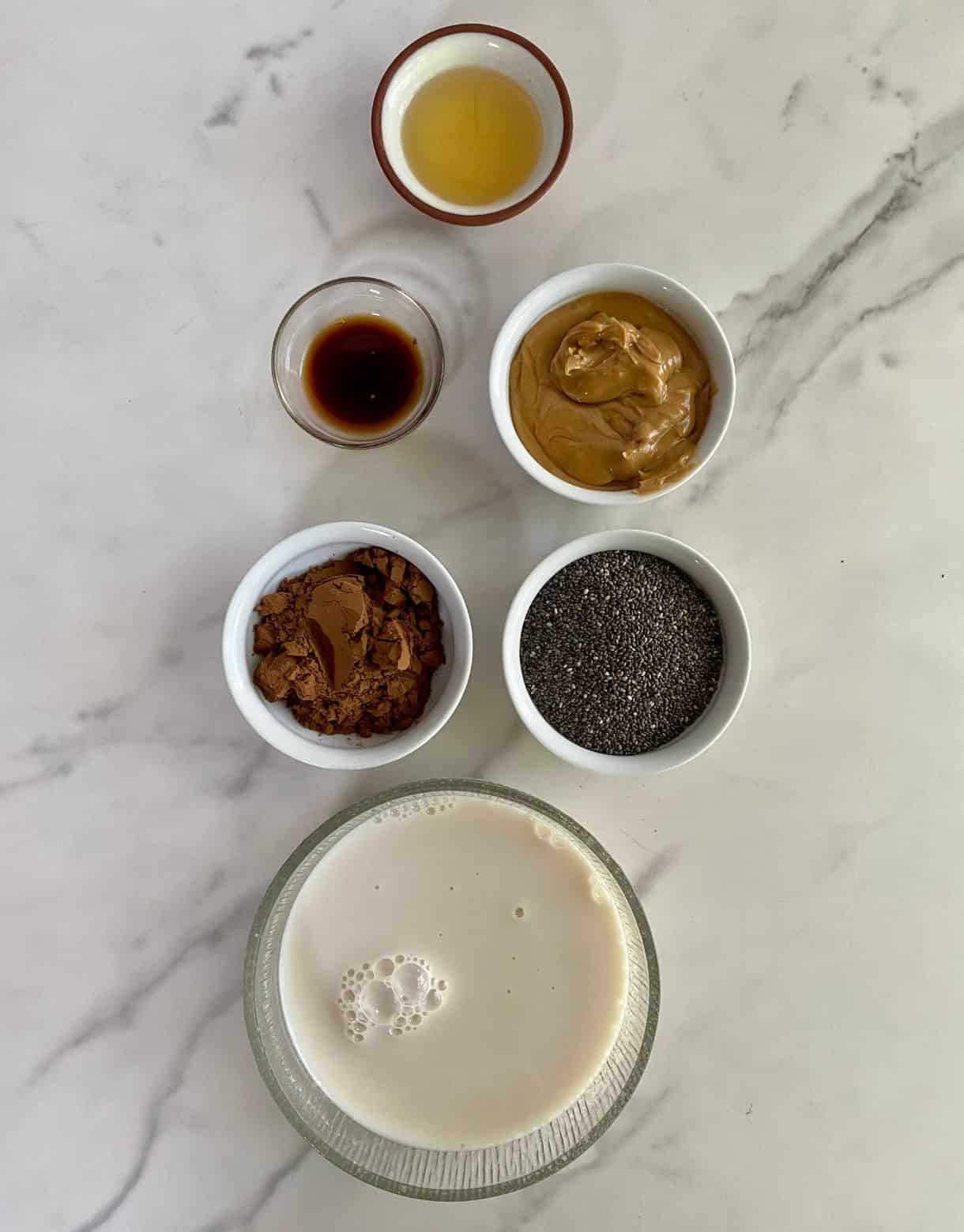 Small bowls of chia seeds, almond milk, cocoa powder, peanut butter, vanilla extract and monk fruit sweetener.