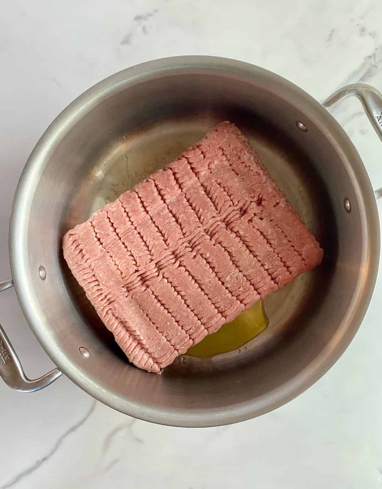 A skillet with olive oil and raw ground turkey.