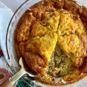 A cooked Ham and Cheese Crustless Quiche in a pie dish cut into 6 pieces with one slice removed.