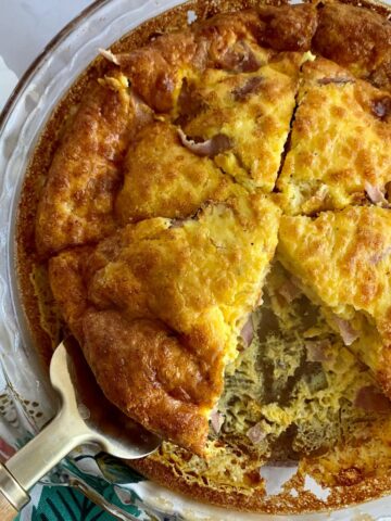 A cooked Ham and Cheese Crustless Quiche in a pie dish cut into 6 pieces with one slice removed.