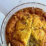 A cooked Ham and Cheese Crustless Quiche in a pie dish cut into 6 pieces with one slice removed.