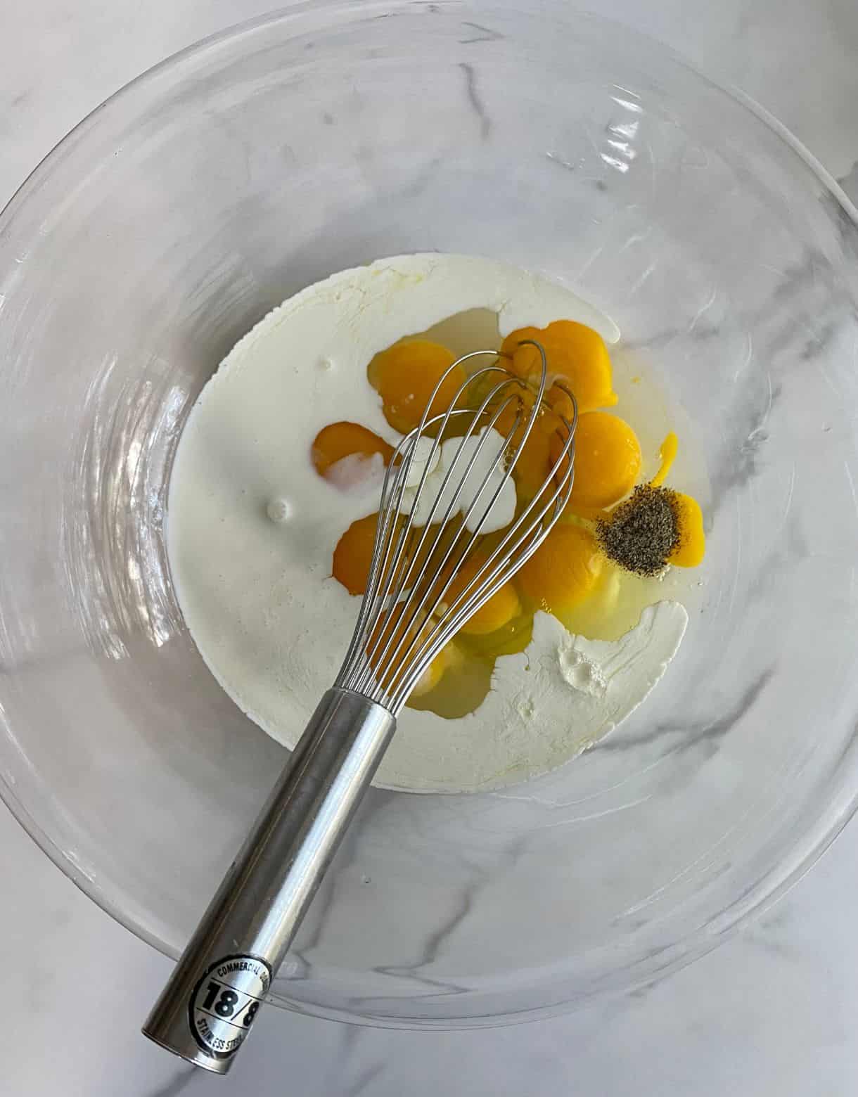 A mixing bowl with eggs, heavy cream, salt and pepper added, but not yet mixed.