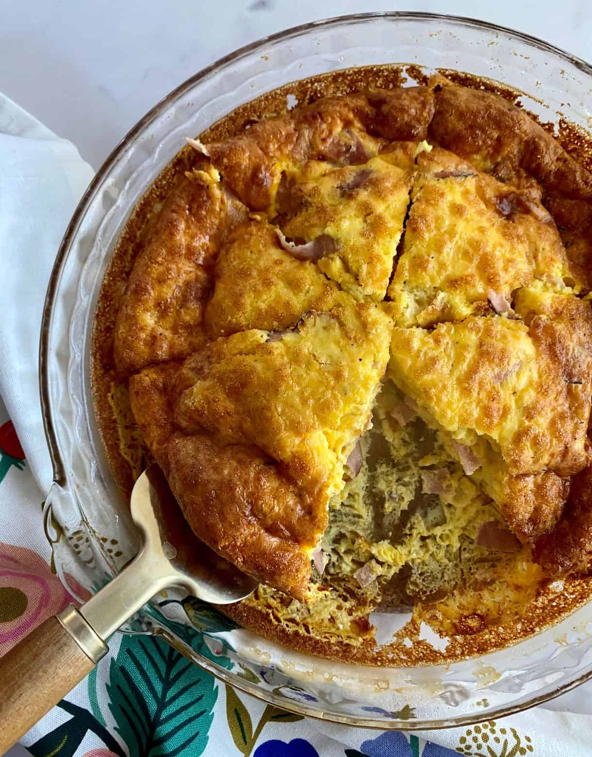 A cooked Ham and Cheese Crustless Quiche in a pie dish cut into 6 pieces with one slice removed.