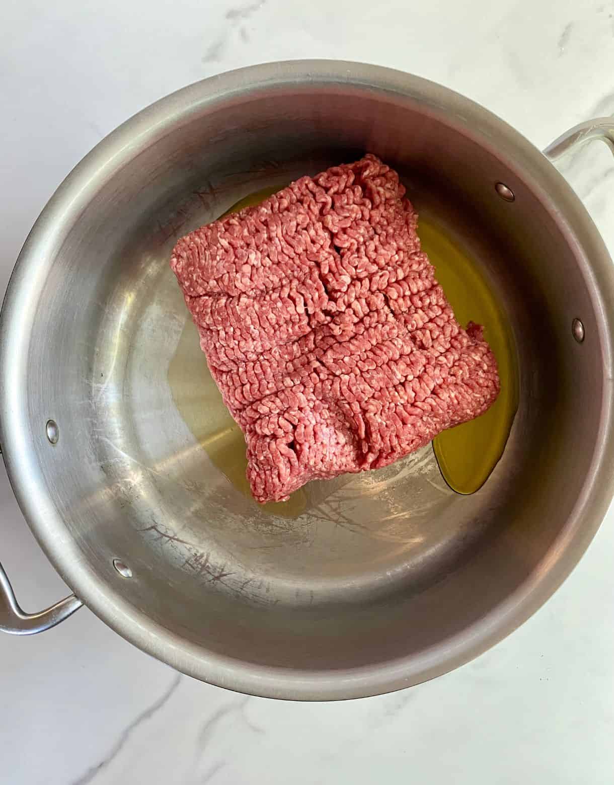 A skillet with olive oil and raw ground beef.