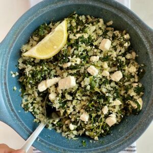 A dish with cooked Mediterranean Cauliflower Rice and a wedge of lemon.