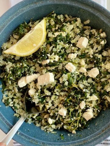A dish with cooked Mediterranean Cauliflower Rice and a wedge of lemon.