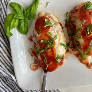 A platter with cooked Pepperoni Pizza Chicken topped with fresh basil.