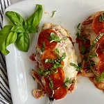 A platter with cooked Pepperoni Pizza Chicken topped with fresh basil.