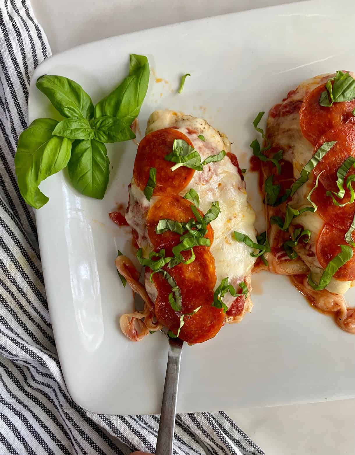 A platter with cooked Pepperoni Pizza Chicken topped with fresh basil.