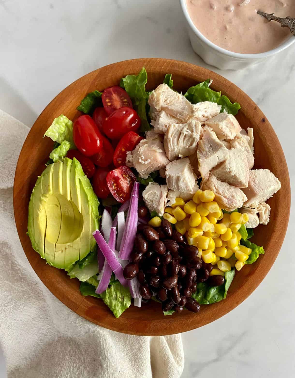 A Santa Fe Chicken Salad in a wooden bowl with a dish of Creamy Salsa Dressing.