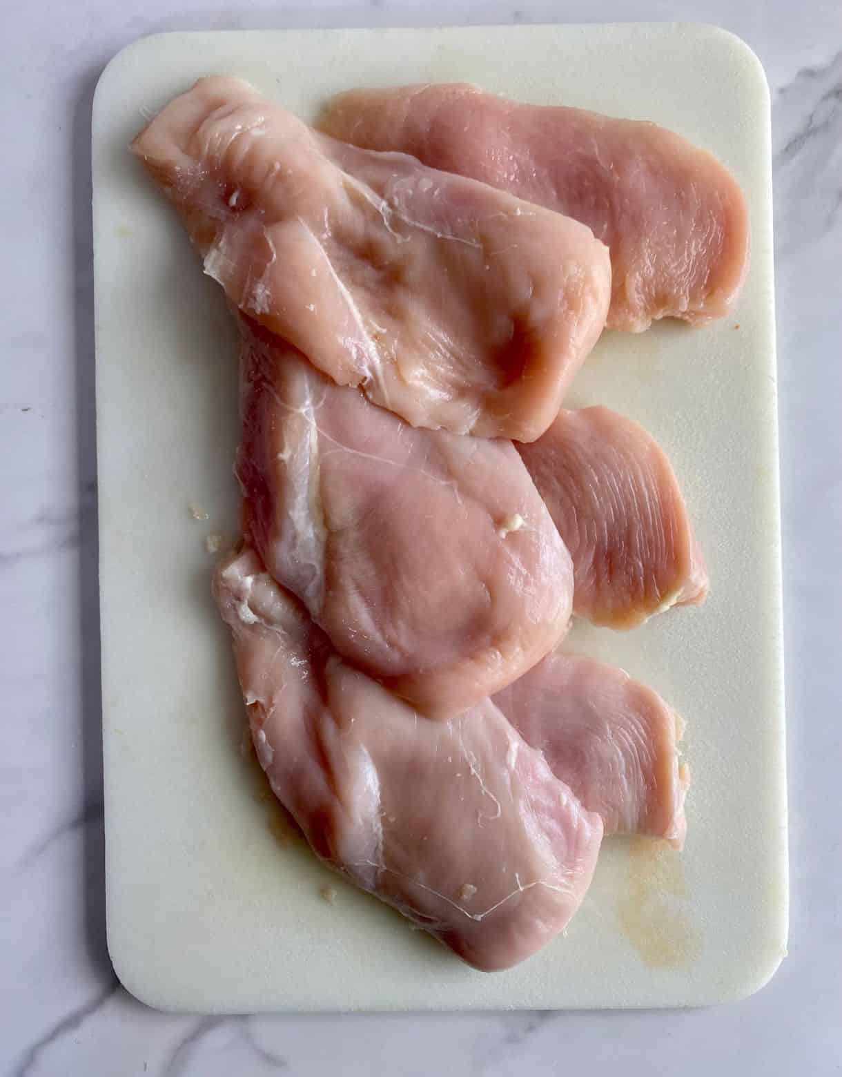 A cutting board with chicken breasts sliced into cutlets.