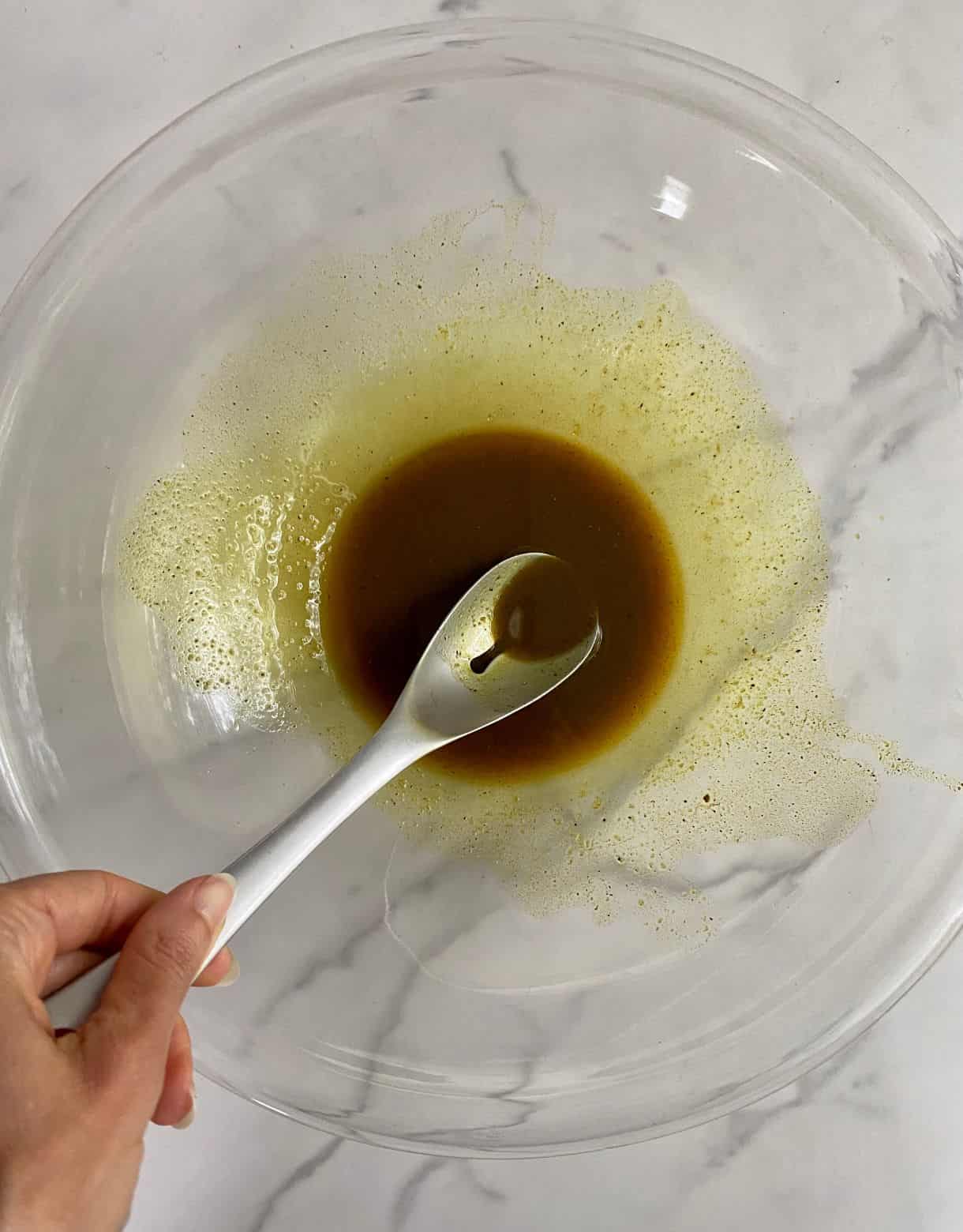 A bowl of oil stirred with spices and a spoon.