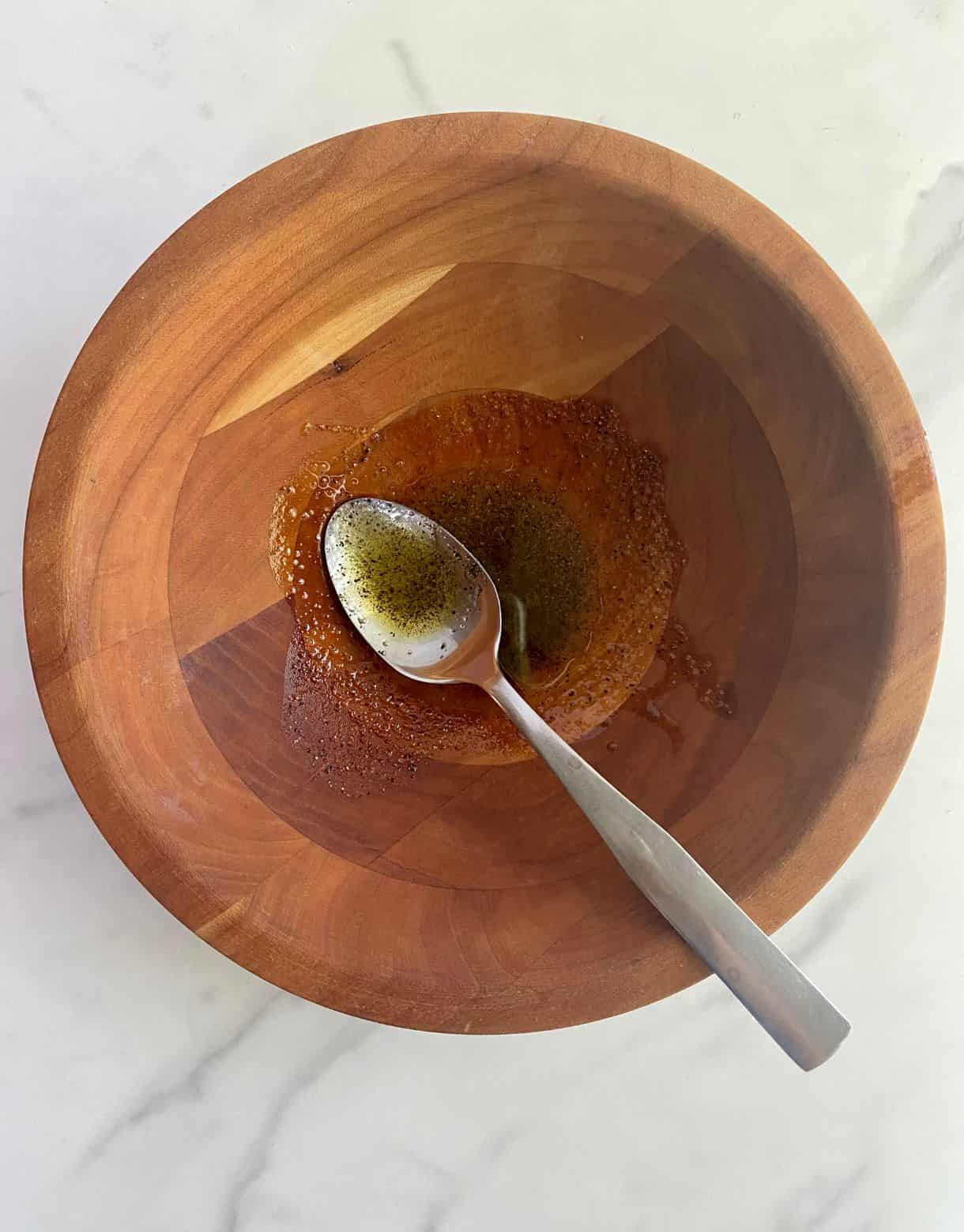 A wood bowl with olive oil, salt and pepper stirred together with a spoon.
