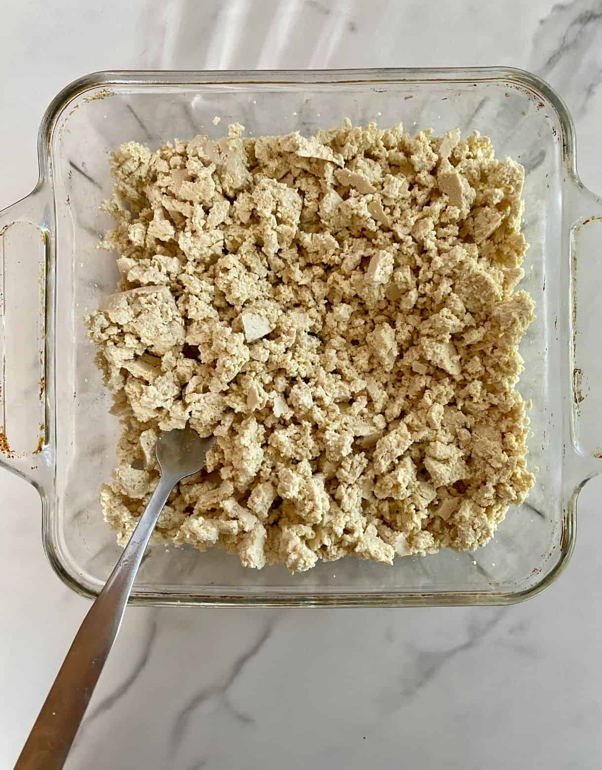 A dish with a block of tofu that has been crumbled.