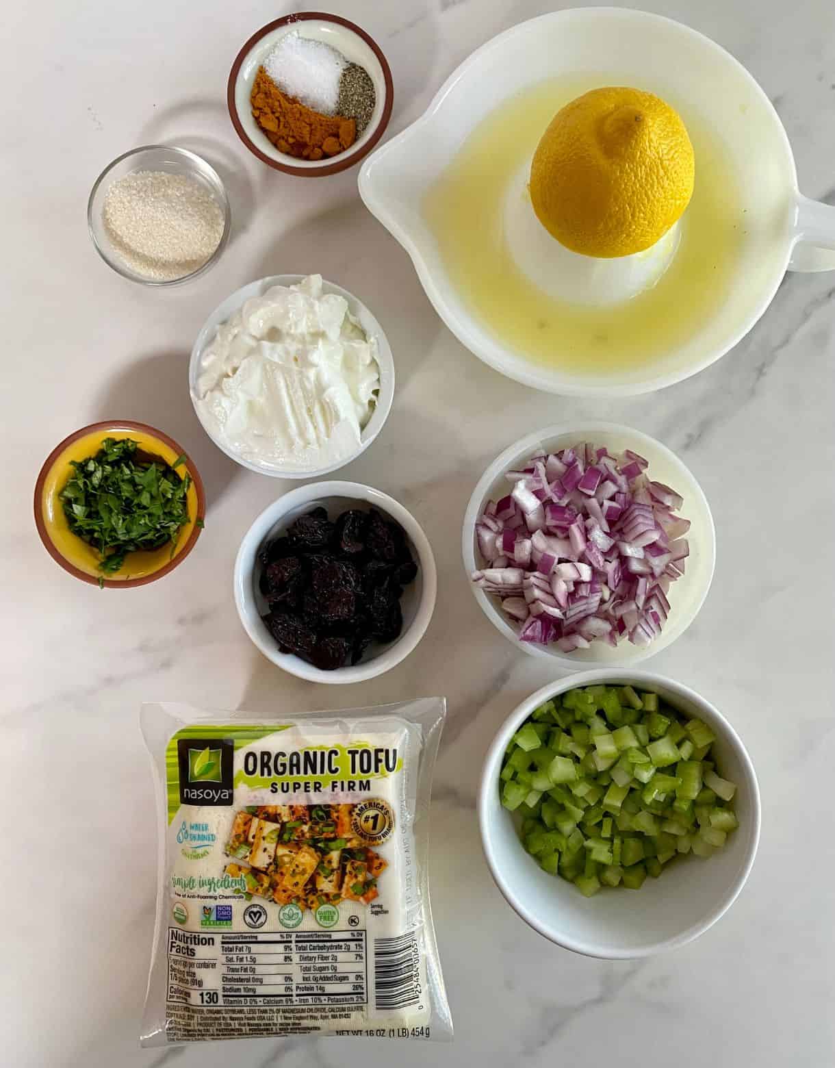 A block of tofu, chopped celery, chopped red onion, lemon juice, dried cranberries, mayonnaise, chopped cilantro, sugar, salt, pepper and curry powder.