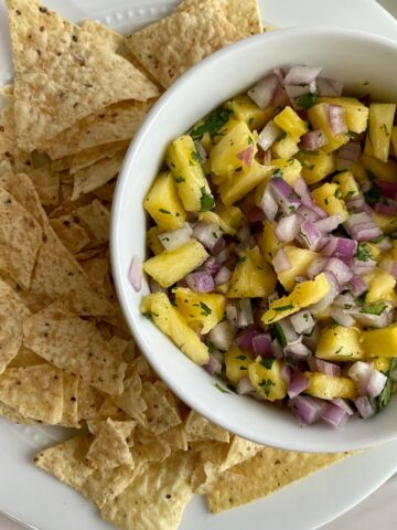 A bowl of Pineapple Pico de Gallo on a plate full of tortilla chips.