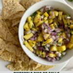A bowl of Pineapple Pico de Gallo on a plate full of tortilla chips.