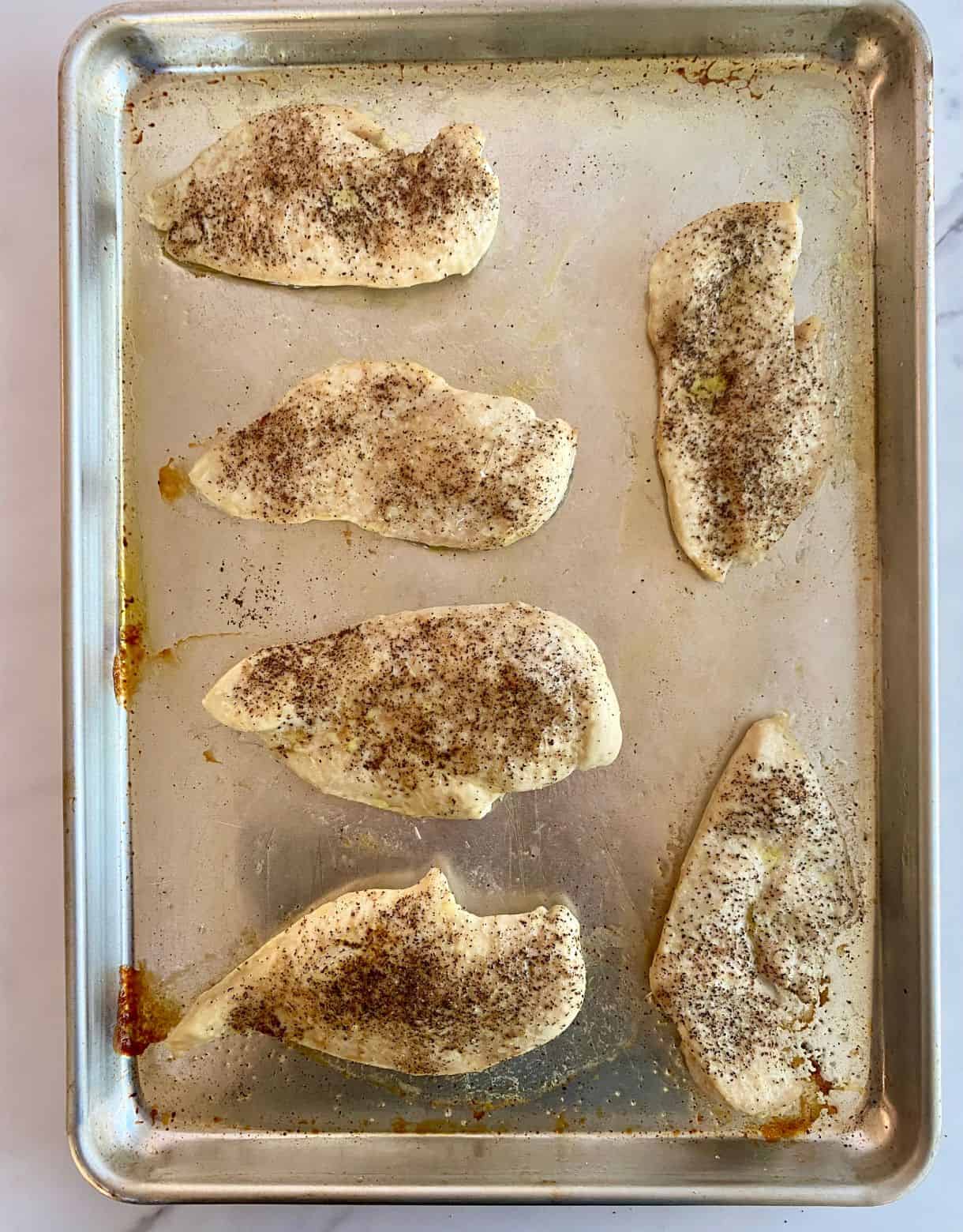 A sheet pan with cooked seasoned chicken cutlets.