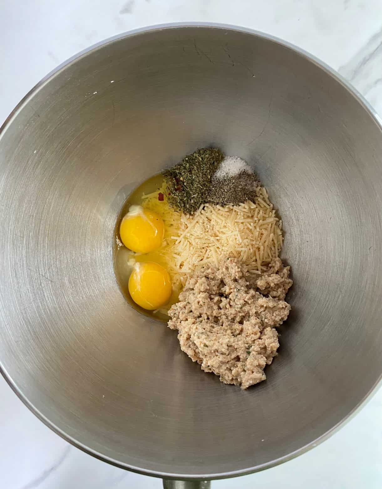 A bowl with milk-soaked bread crumbs, parmesan cheese, two eggs and spices ready to be mixed.