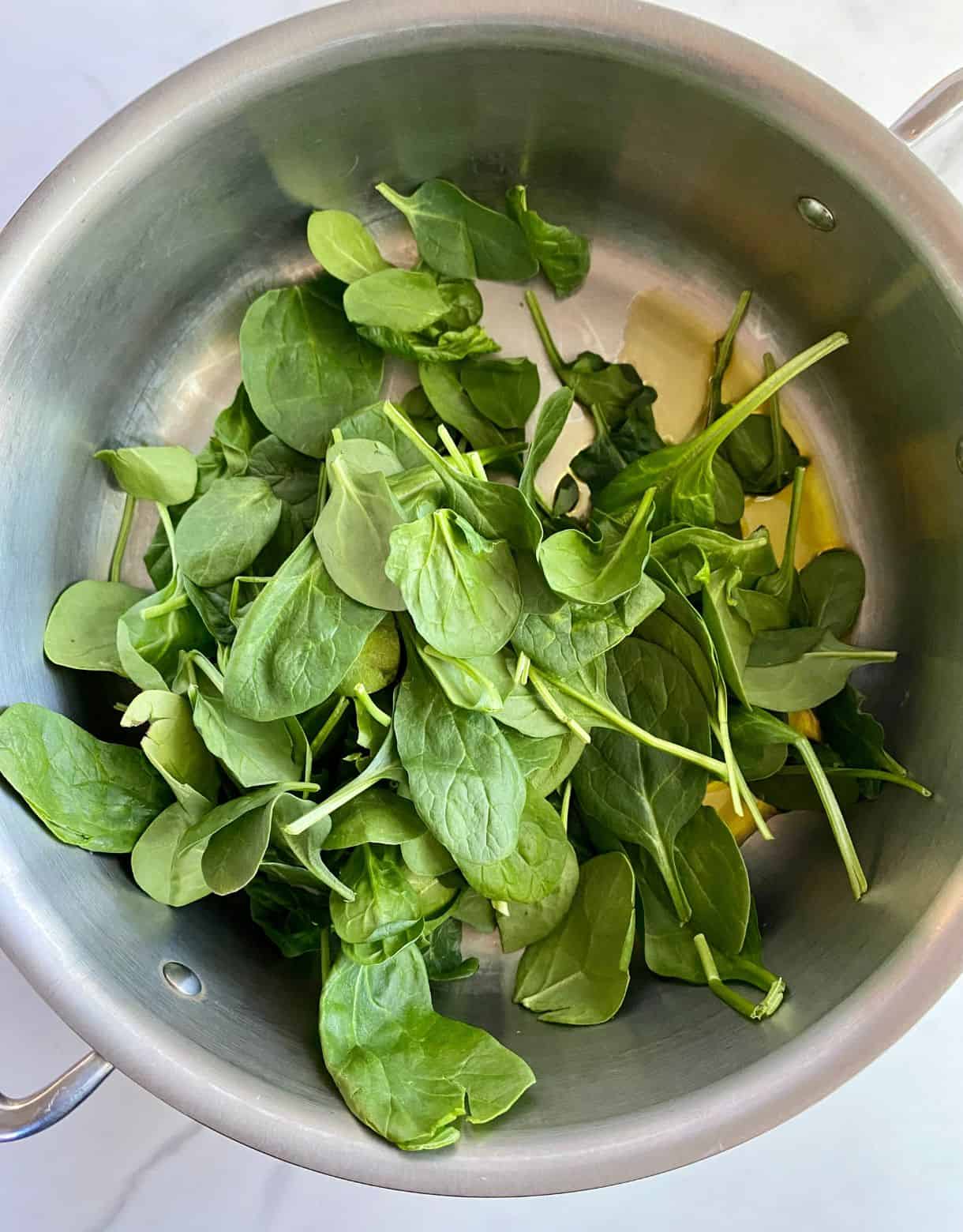 A pan with olive oil and raw spinach.