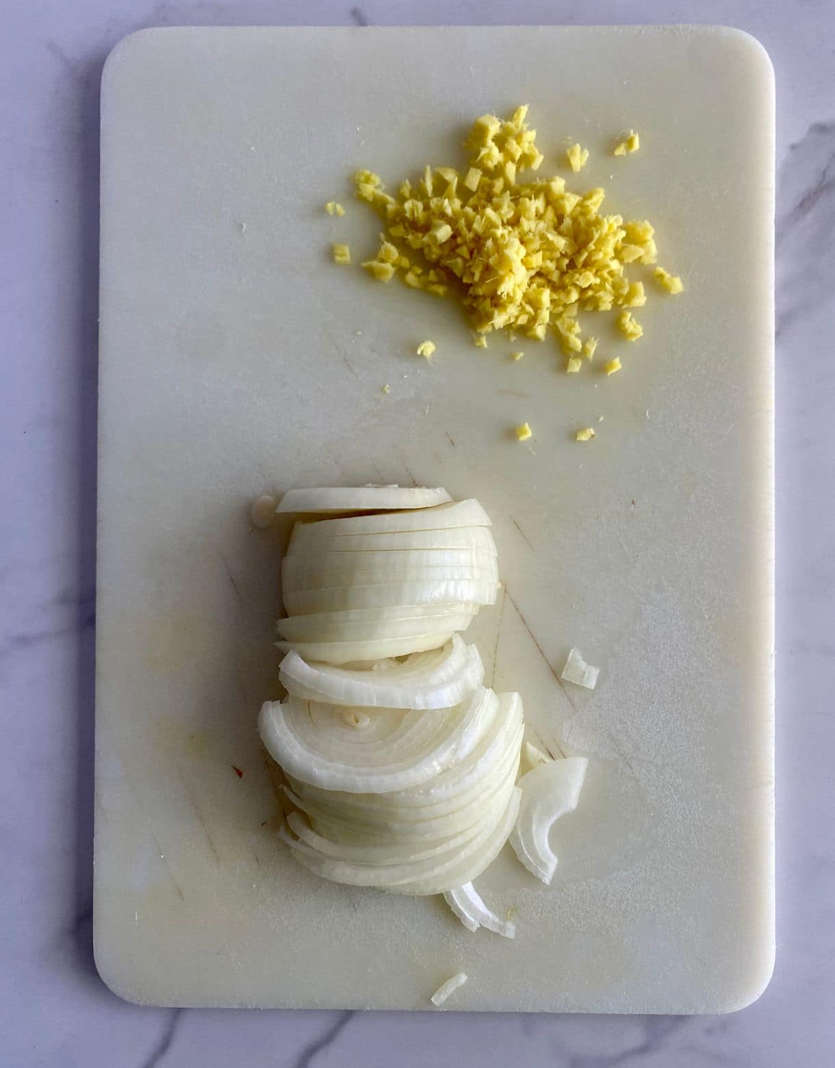A cutting board with a sliced onion and minced ginger.