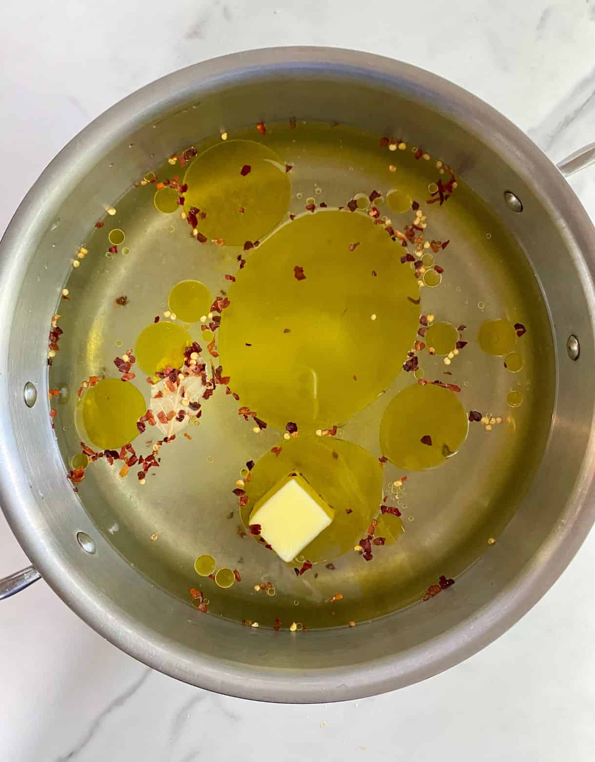 A pot with white wine, water, butter, olive oil, lemon juice, sugar and spices added to it.