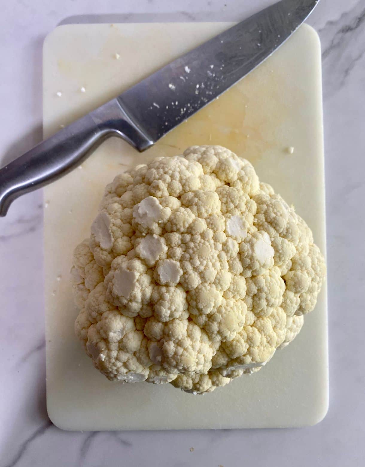 A cutting board, a knife and a head of trimmed cauliflower.