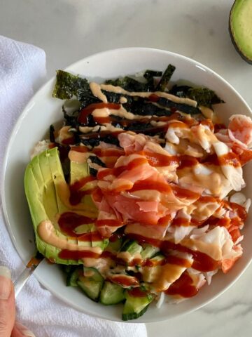 A Deconstructed Sushi Bowl with cauliflower rice, crab, avocado, cucumbers, seaweed, pickled ginger and sriracha mayo.