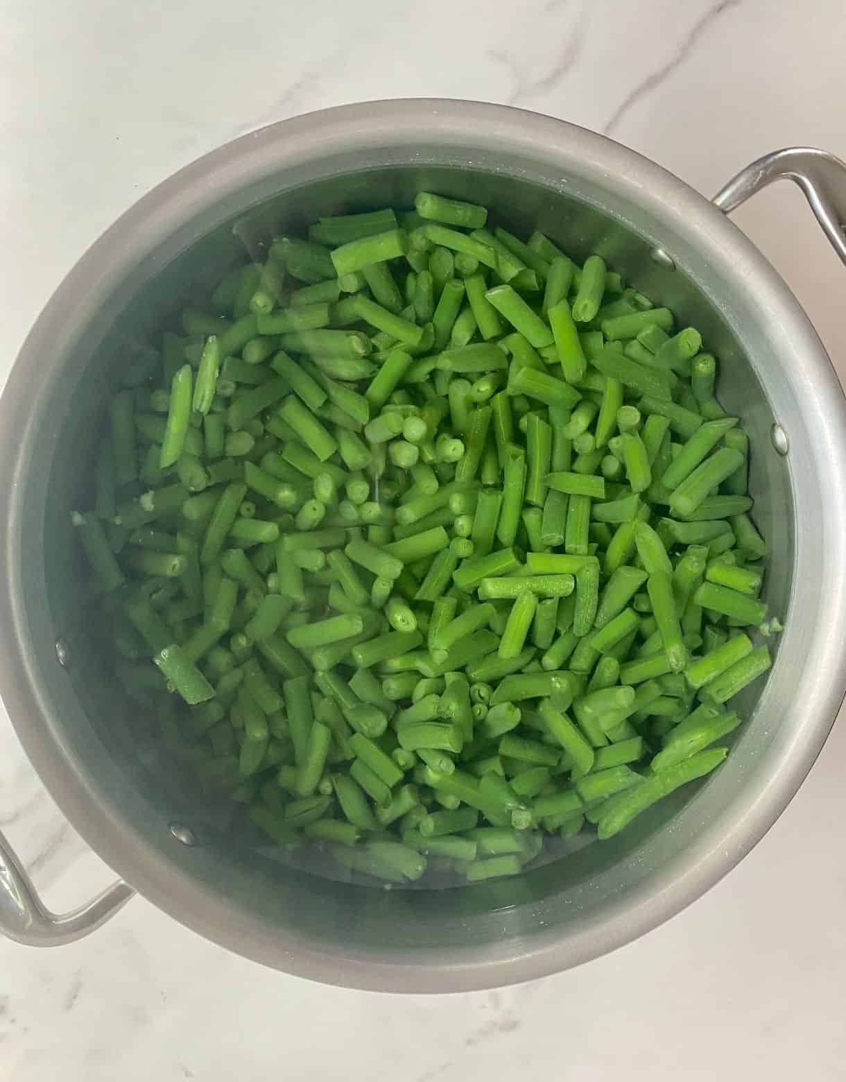A pot of water with green beans simmering.