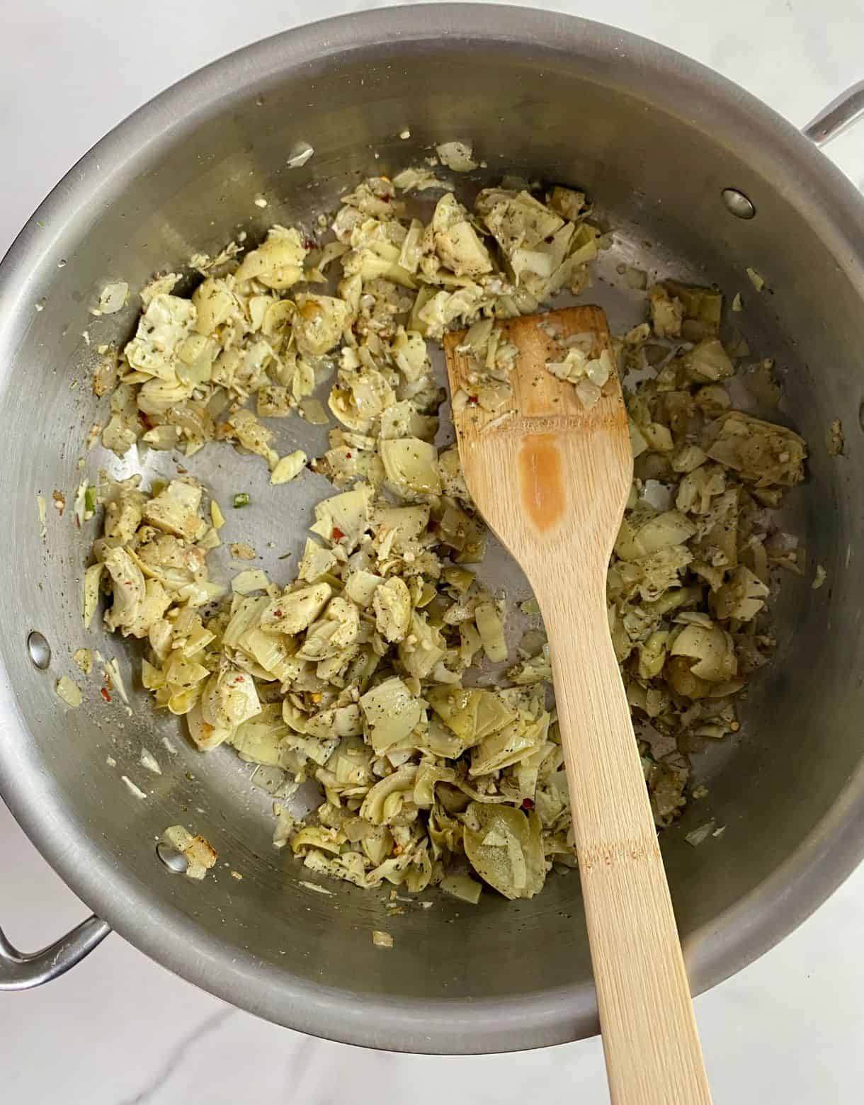 A pot of sauteeing onions and artichoke hearts.