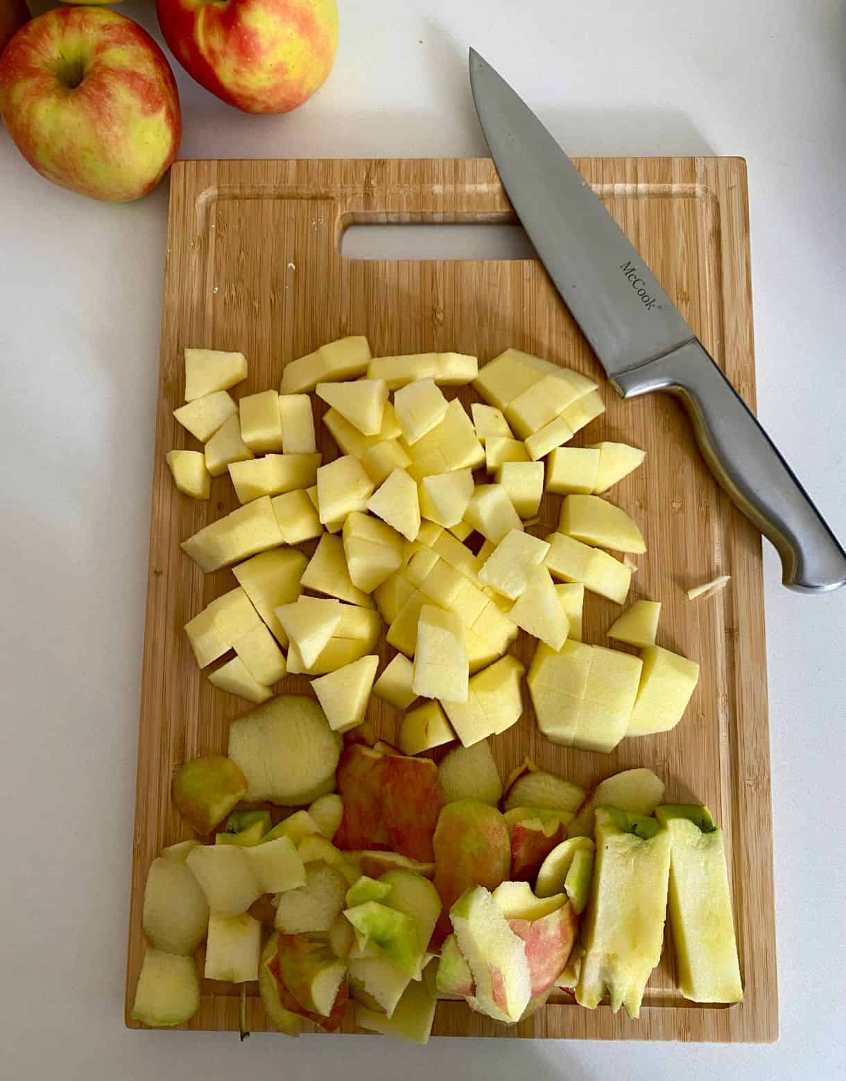 A cutting board with a knife and diced and peeled apples.