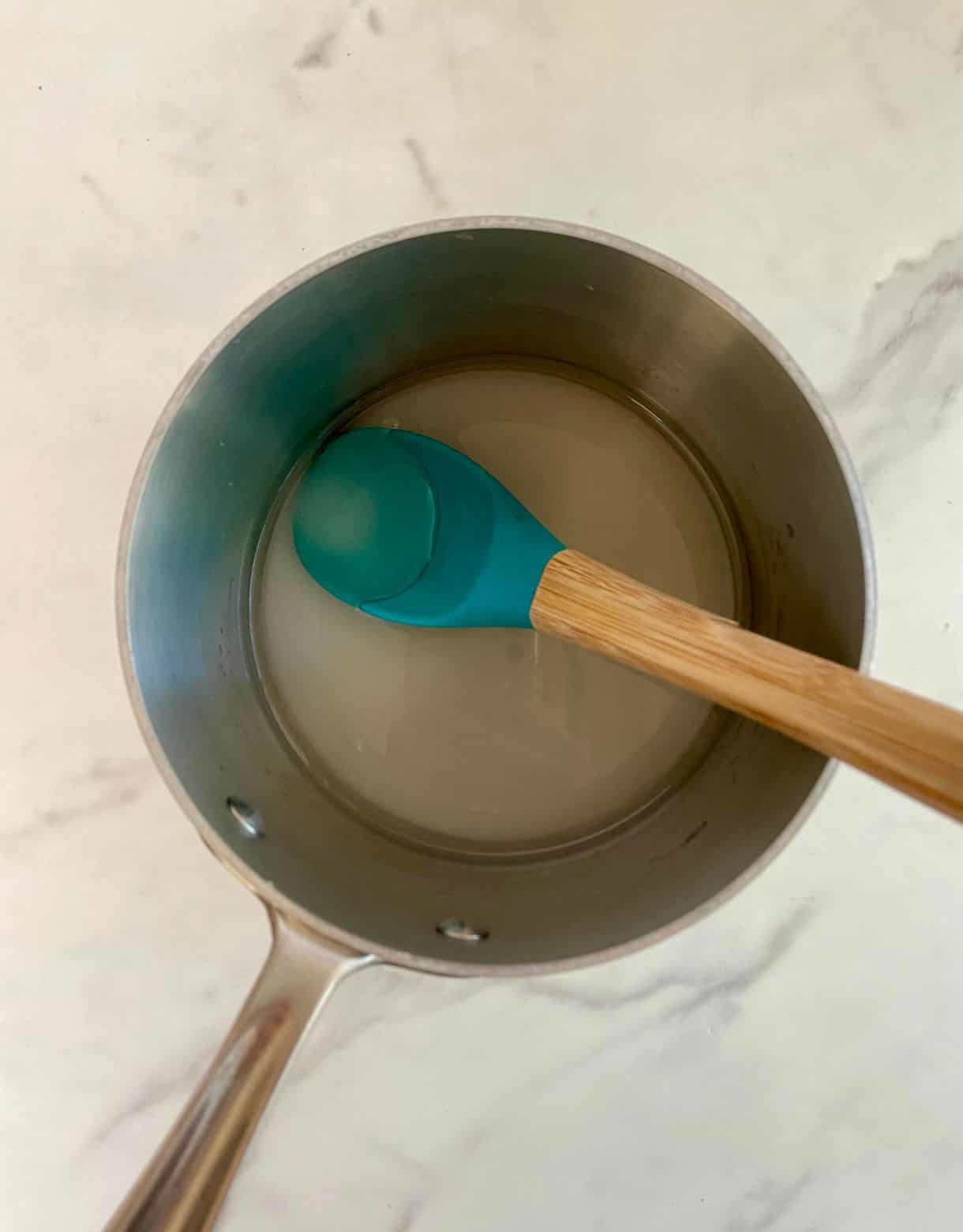 A small sauce ot with sugar, water, and a spoon.