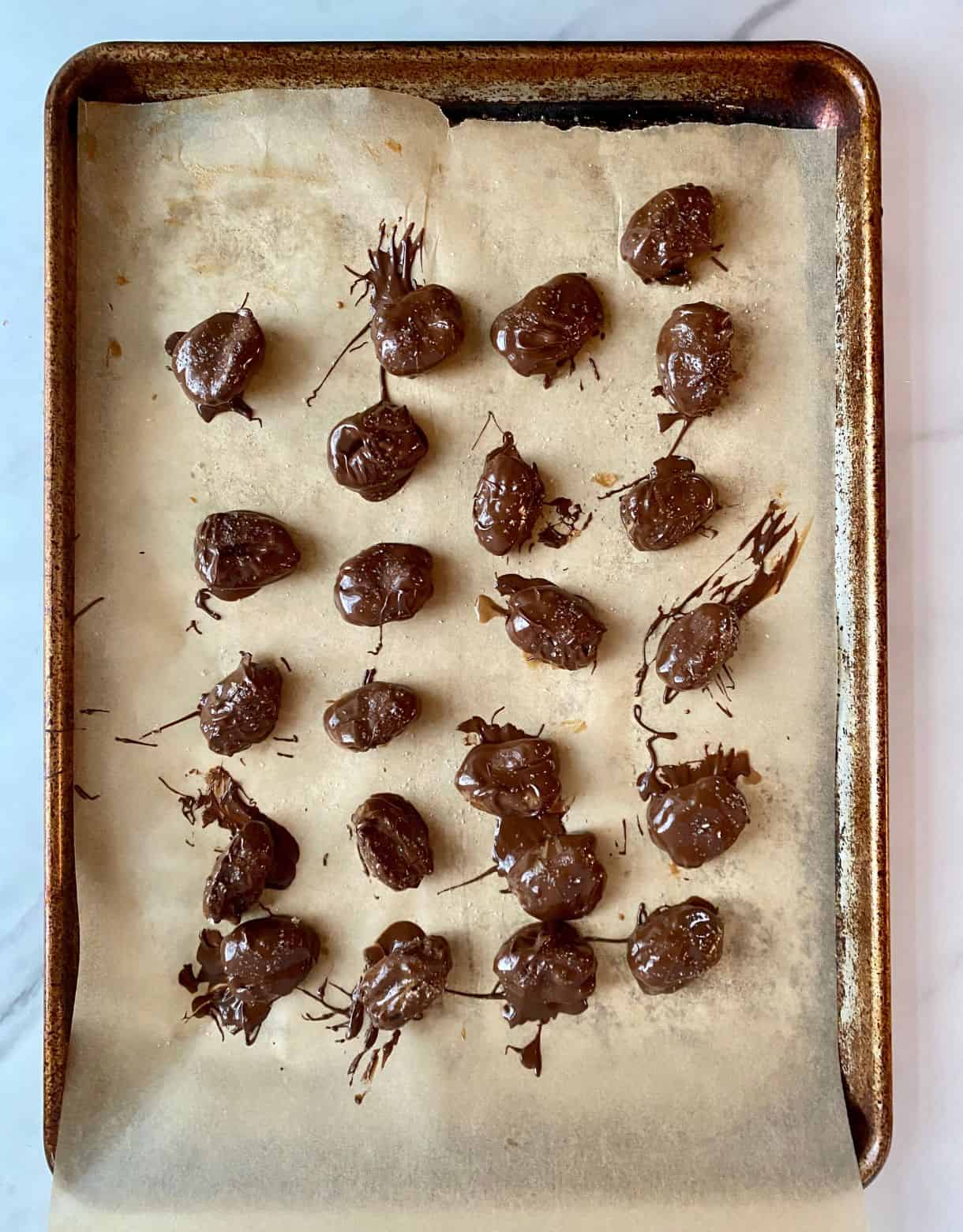 A pan lined with parchment paper with dates that have been dipped in chocolate.