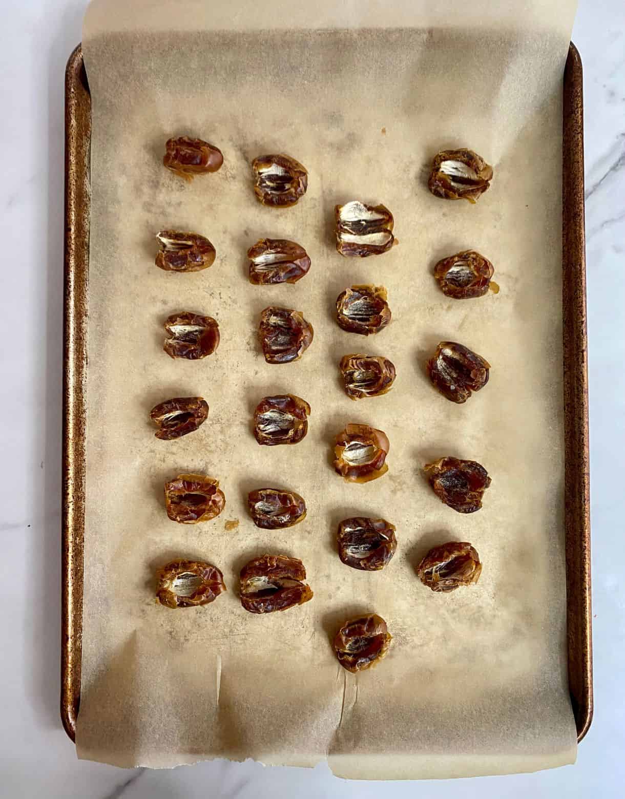 A pan lined with parchment paper with dates that have been pitted.