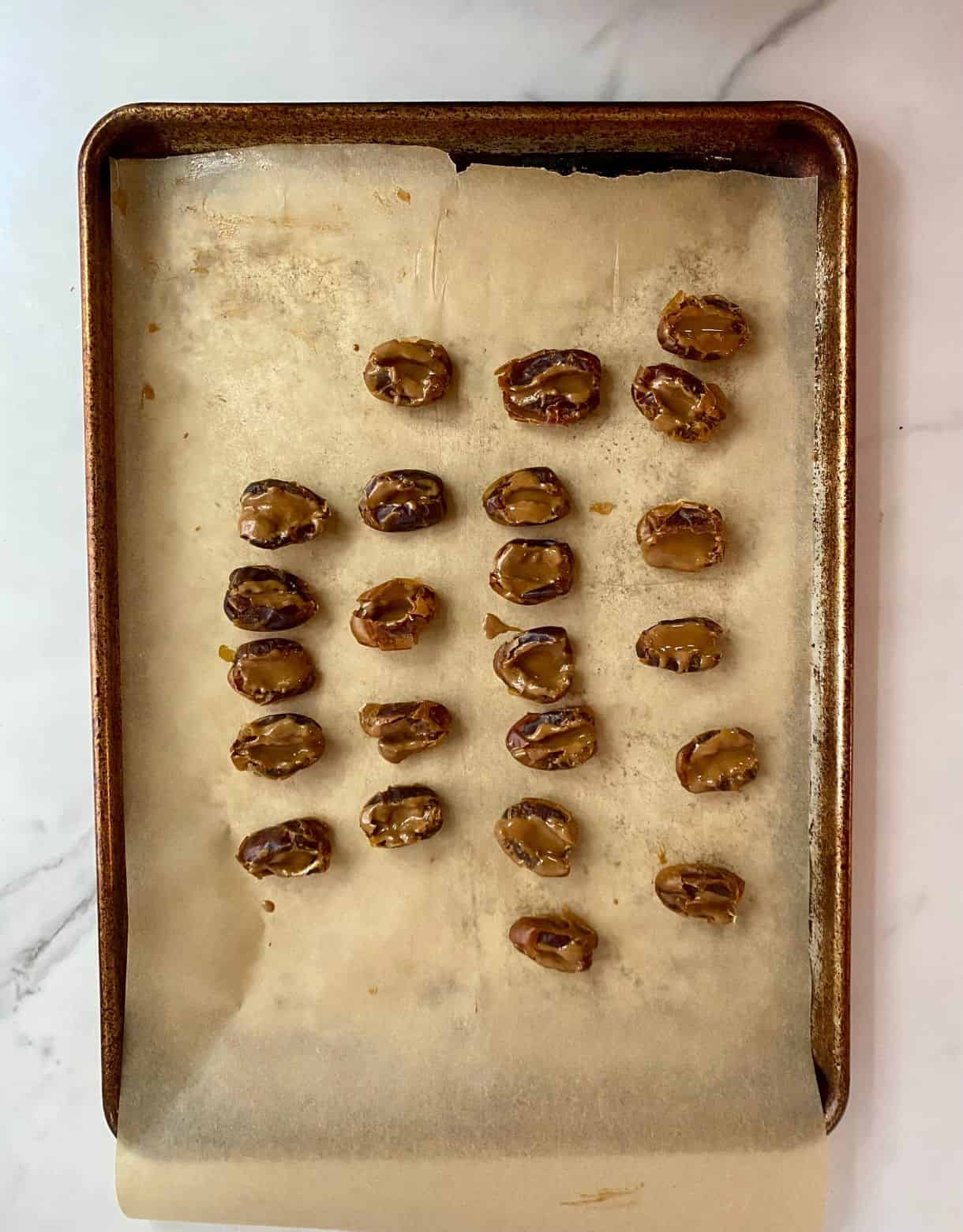 A pan lined with parchment paper with dates that have been stuffed with almond butter.