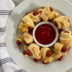 A platter of cooked little smokies pigs in a blanket with ketchup.