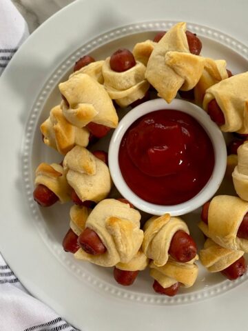 A platter of cooked little smokies pigs in a blanket with ketchup.