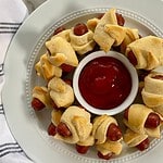 A platter of cooked little smokies pigs in a blanket with ketchup.