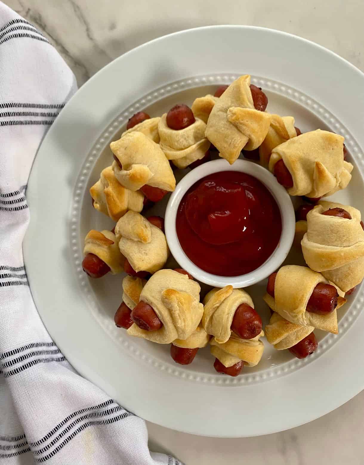 A platter of cooked little smokies pigs in a blanket with ketchup.