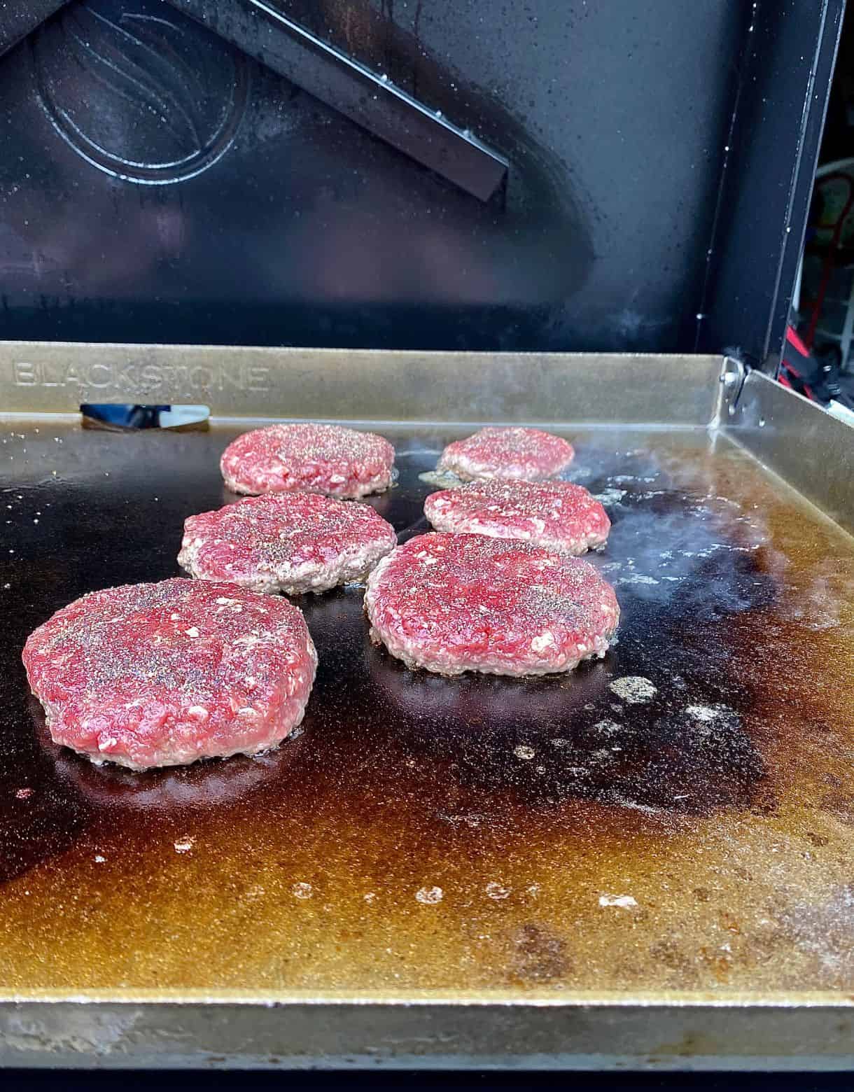 Six venison burgers cooking on a grill.