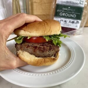 A cooked Venison Burger on a bun with arugula and tomato.